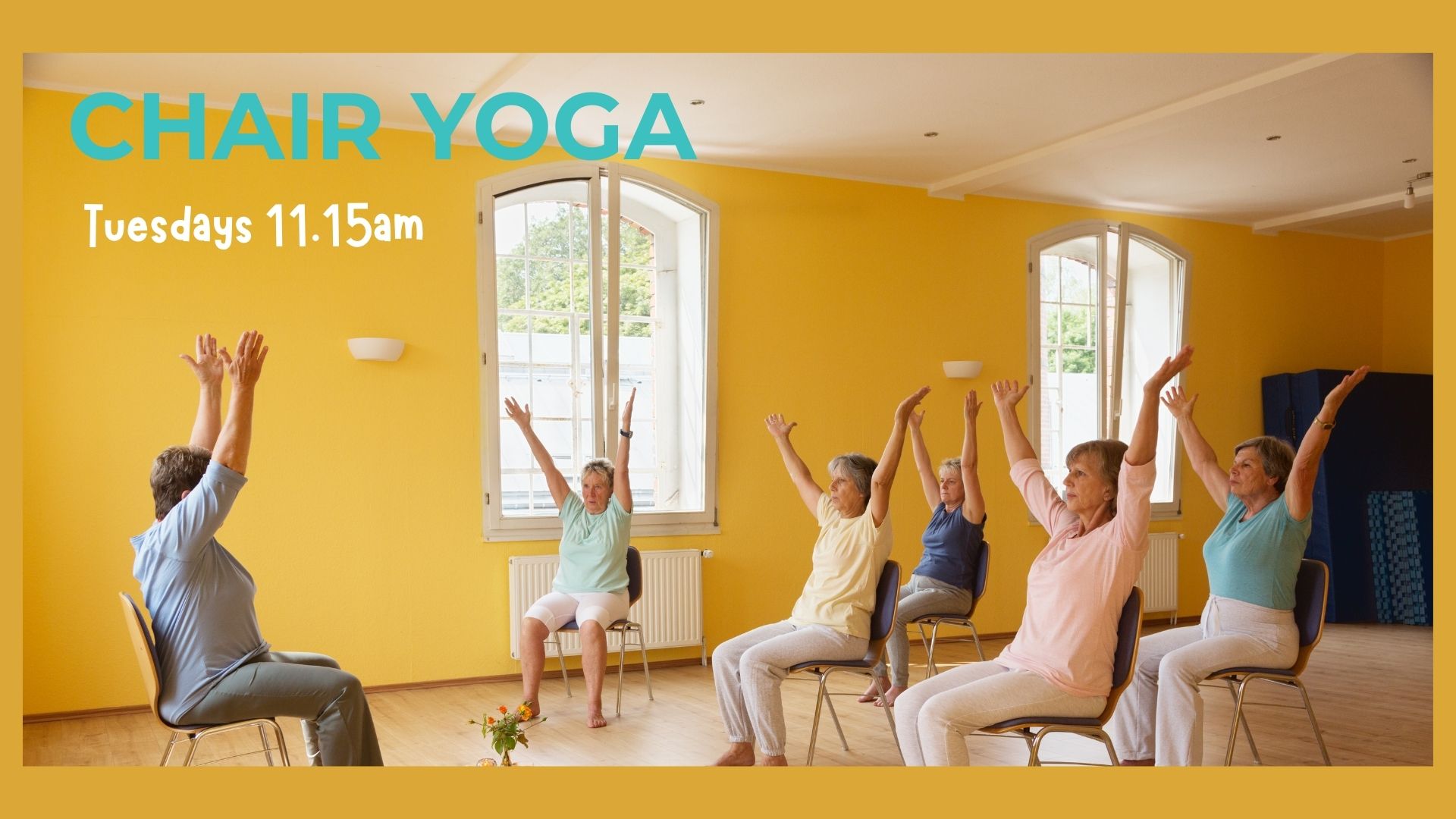 5 ladies sitting on chairs taking part in a chair yoga session. The instructor sits in front of them demonstrating. The walls are yellow with two large windows. The floor is wood.